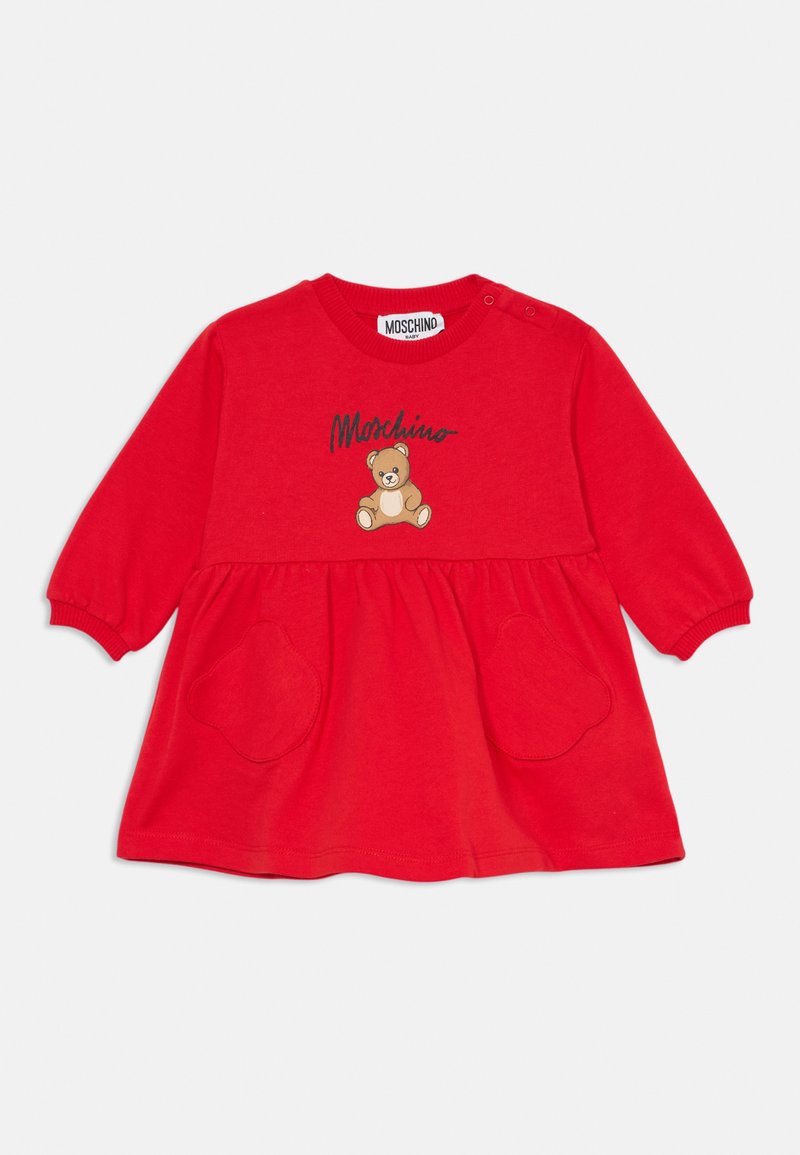 Κόκκινο βαμβακερό φόρεμα με μακριά μανίκια, στρογγυλή λαιμόκοψη, γραφικό αρκουδάκι και δύο τσέπες σε σχήμα καρδιάς στη μέση, με ετικέτα μάρκας στο επάνω μέρος.