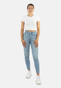 Helle blaue hochgeschnittene Jeans mit slim fit, kombiniert mit einem weißen, cropped T-Shirt. Weiße Sportschuhe runden das Outfit ab.