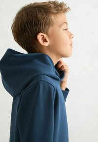 Tmavě modrá mikina s kapucí, prostornou kapucí, hladkou texturou a volným střihem. Boční pohled se zaměřuje na výstřih a design ramen.