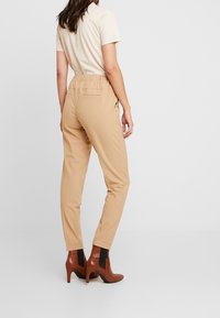 Beige Hosen mit schmalem Schnitt und elastischem Bund, kombiniert mit braunen Stiefeletten mit Absatz und schwarzen seitlichen Einsätzen.