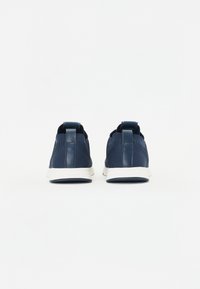 Navy blue sneakers feature a textured fabric upper, a smooth leather heel tab, and a white rubber sole with a patterned tread.