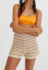 I pantaloni corti all'uncinetto presentano strisce multicolori (arancione, viola, giallo) con un bordo in pizzo. Coulisse regolabile in vita. Materiale a maglia leggero.