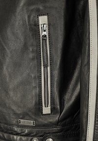 Svart lädermotorcykeljacka med en silverfärgad dragkedjeficka, grå detaljer, sömnadsdetaljer och metallisk hårdvara.