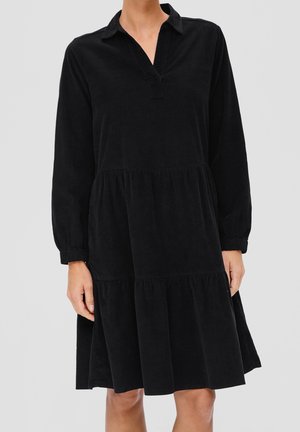 Czarna sztruksowa sukienka z kołnierzykiem, długimi rękawami i suknią w kilku warstwach. Posiada dekolt w kształcie litery V oraz marszczone mankiety przy nadgarstkach. Miękka w dotyku.