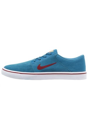 Niebieski niski sneaker z czerwonym logo Nike, białą podeszwą z czerwonym paskiem i niebieskimi sznurowadłami, pokazany z boku na białym tle.
