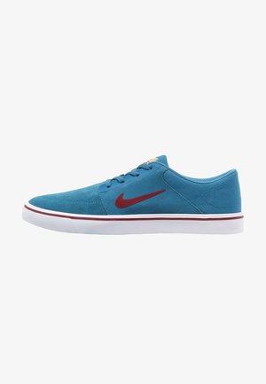 Sneaker blu low-top con swoosh Nike rosso, suola bianca con striscia rossa e lacci blu, mostrato di lato su sfondo bianco.