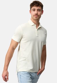 Lys beige kortærmet polo shirt med en klassisk krave, ribbet struktur og et lille logo på brystet. Har sideslidser for komfort.