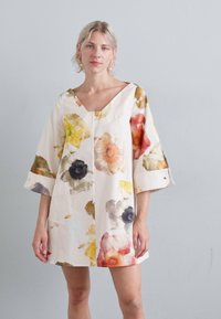 Vestido floral con escote en V, mangas tres cuartos y un corte holgado. Base blanca con patrones de flores coloridas en naranja, amarillo y negro.