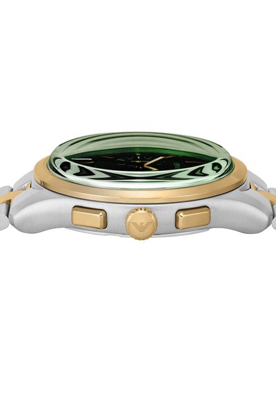 Kulaté hodinky s zeleným skleněným kupolem, zlatými akcenty, černým ciferníkem a pouzdrem z nerezové oceli. Obsahují dvě tlačítka a texturovanou korunku.