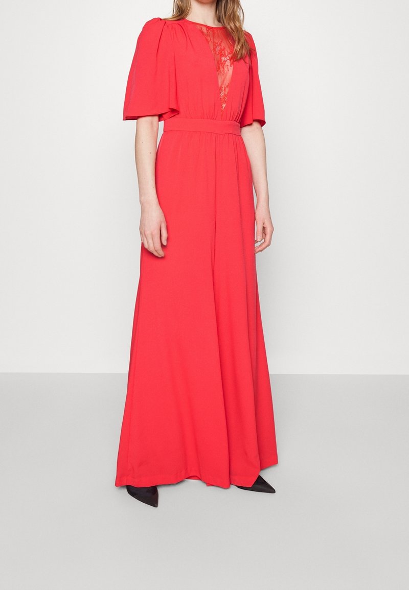 Maxi dress in bright red fabric with short puff sleeves and lace detailing at the neckline, featuring a fitted waist and flowing bottom.