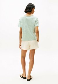 Gestreepte groen en witte overhemd met korte mouwen, relaxte pasvorm, gecombineerd met crèmekleurige shorts. Getextureerde stof, casual stijl en platte sandalen zichtbaar.