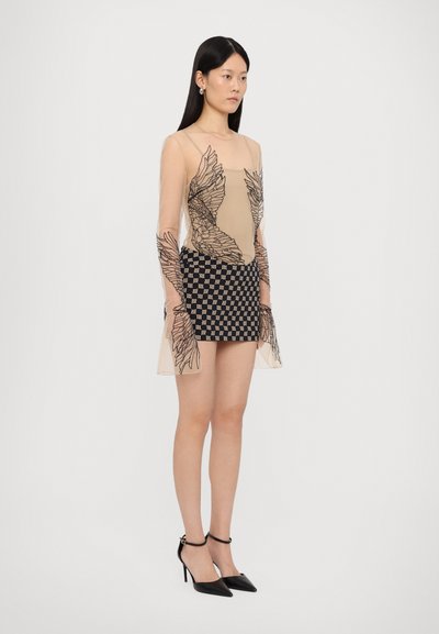 Top nudo a maniche lunghe con ricami floreali neri, abbinato a una mini gonna a scacchi bianca e nera e scarpe con tacco nere.