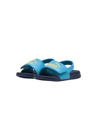 Blauwe en marineblauwe Puma-slippers met verstelbare banden en een gele Puma-logo bovenop, ontworpen voor casual gebruik en comfort.