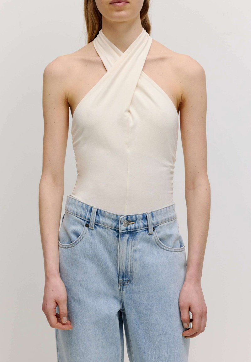 Crème-kleurige halterbodysuit met een kruis-over halslijn, gecombineerd met lichtblauwe, high-waisted spijkerbroeken met stikseldetails en zakken.