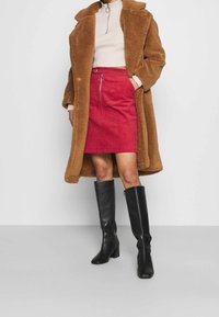 Brun faux fur frakke, cremet ribbet top, rød fløjlsnederdel med lynlås foran og knæhøje sorte læderstøvler med hæl. Ensfarvet farveskema.