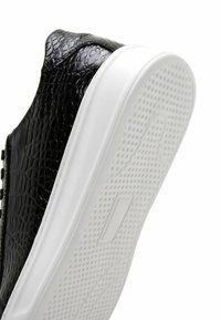 Sneaker nero con texture in rilievo simile a quella di un rettile, dotato di suola in gomma bianca e texture a punto per garantire aderenza. Vista laterale.