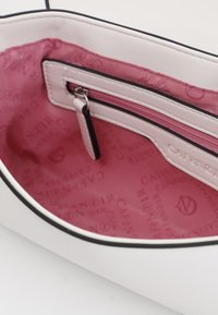 Interno di una borsa bianca con texture liscia, dotato di una fodera in tessuto rosa incisa con il nome del marchio e una tasca con zip.