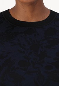 Mörkblå tröja med ribbad svart halsringning och ett subtilt blommönster i en något mörkare nyans. Tyget ser texturerat ut.