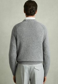 Grå stickad tröja med ribbad krage och mudd, med subtila horisontella sömmar längs axlarna. Bärs med ljusgrå rutiga byxor.