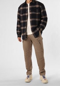 Kostkovaná flanelová košile v námořnické modři, hnědé a šedé; béžové cargo kalhoty; krémové tričko; béžové tenisky s námořnickými a červenými akcenty.