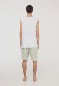 Top bianco senza maniche abbinato a pantaloni corti chiari con stampa di banane. Il tessuto sembra morbido con una vestibilità rilassata.