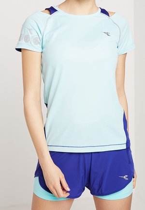 Lyseblå sports t-shirt med korte ærmer, der har skulderudskæringer og marineblå detaljer. Indeholder et dekorativt grafik nær skulderen.