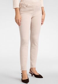 Jeans ajustados beige claro con una textura suave, que cuentan con bolsillos frontales y una cinturilla elástica para mayor comodidad. Combinados con tacones marrón oscuro.