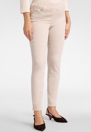 Jeans skinny beige chiaro con una texture liscia, dotati di tasche anteriori e una vita con elastico per il comfort. Abbinati a tacchi marrone scuro.