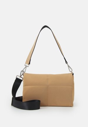 Tan cylindrical bag made of soft material, featuring a black adjustable strap, silver hardware, and a quilted texture.