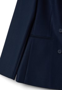 Blazer azul marino con una textura suave, que cuenta con dos botones, un bolsillo en el pecho y bolsillos laterales con un ajuste entallado.