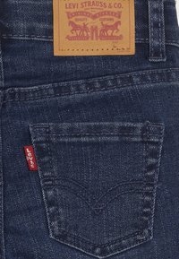 Jeans de mezclilla en azul oscuro con una pequeña etiqueta roja de Levi's en el bolsillo trasero. Presenta un diseño de bolsillo distintivo con costuras y etiqueta de cuero.