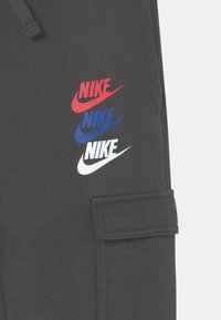 Gray sweatpants made of cotton blend featuring three stacked Nike logos in red, blue, and white. Includes side pocket detail.