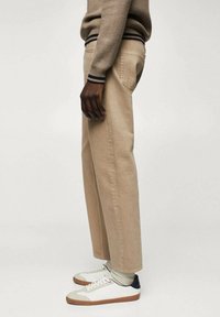 Beige Baumwollhosen mit geradem Schnitt und Gesäßtaschen, kombiniert mit weißen und grauen Sneakers mit strukturierten Sohlen und dunkelblauen Akzenten.