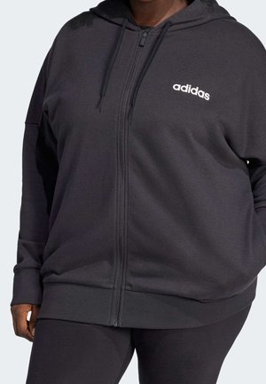 Osoba nosząca czarną bluzę Adidas z pełnym zamkiem błyskawicznym, kapturem i białym logo na piersi, w połączeniu z czarnymi spodniami.