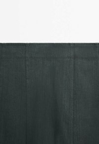 Gros plan d’un tissu gris foncé avec des coutures verticales et horizontales visibles formant des panneaux rectangulaires.