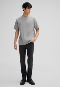 Lichtgrijze t-shirt met korte mouwen en een ronde hals, gedragen met donkere jeans en zwarte laarzen. Eenvoudig, ontspannen pasvorm ontwerp.