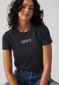 Melna kokvilnas T-kreklu ar apaļu kaklu, uz kura priekšpusē centrā ir balts "LEVI'S" logo, pieguļošas piedurknes un gluda tekstūra.