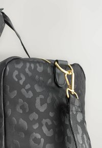 Taška s leopardím potiskem v černé barvě, s hladkou texturou, zlatými kovovými detaily a pevným popruhem. Obsahuje zlatý zip na vrchu.