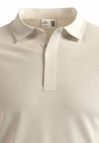 Polo shirt beige chiaro in tessuto testurizzato, con colletto e due bottoni. Etichetta con i dettagli del marchio visibile all'interno.