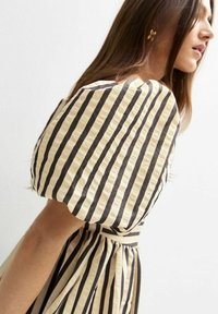 Vestido con mangas abullonadas en crema y rayas negras, con una cintura ajustada y tela texturizada. Diseñado con una silueta fluida.