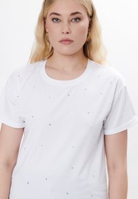 Camiseta blanca de algodón, con cuello redondo y mangas cortas, adornada con pequeños strass dispersos para un detalle especial.