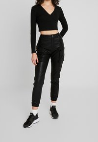 Schwarzes geripptes Crop Top mit V-Ausschnitt, kombiniert mit hochtaillierten schwarzen Cargo-Hosen aus Kunstleder, die Seitentaschen und tapered Cuffs haben.