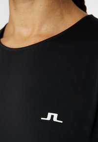 T-shirt de sport noir avec un col rond et une texture lisse, accentué par un logo blanc sur la poitrine.