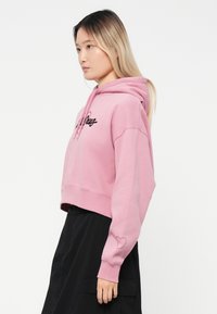 Felpa rosa cropped con maniche lunghe, caratterizzata da testo ricamato nero e un dettaglio a forma di cuore sulla manica. Realizzata in morbido tessuto di cotone misto.