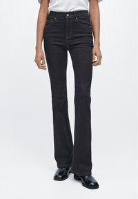 Černé rozšířené džíny s vysokým pasem, pětipokládkovým designem, kontrastním prošíváním a zakončenými lemy. Nosit s černými kotníkovými botami.