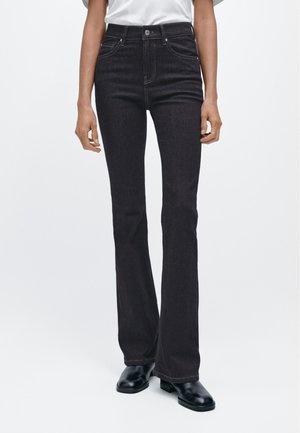 Zwarte jeans met wijde pijpen en een hoge taille, voorzien van een ontwerp met vijf zakken, contrasterend stiksel en afgewerkte zoom. Gecombineerd met zwarte enkellaarsjes.