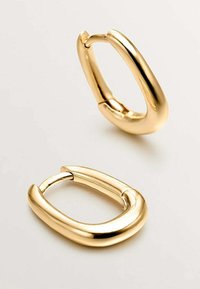 Pendientes de aro en tono dorado con una forma ovalada y gruesa. Superficie suave y pulida con cierre de bisagra. Diseño reflectante y sin costuras.