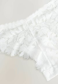 Hvide blonde trusser med blomstermønster, bølgede kanter og gennemsigtig tekstur. Let og delikat design for en glat pasform.