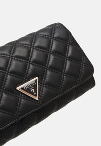 Portafoglio nero trapuntato in pelle, con un accento metallico a logo triangolare. La superficie presenta una finitura testurizzata con quadrati cuciti.
