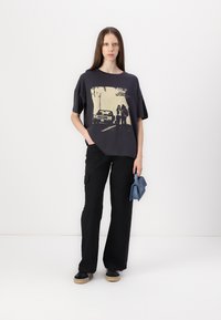 Černé oversized tričko s grafickým potiskem, doplněné černými cargo kalhotami. Ležérní outfit doplněný černými botami a modrou kabelkou.